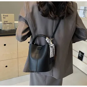 Detail of black lychee grain leather bucket bag with patterned silk scarf on model