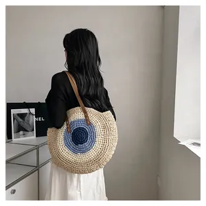Detail of round straw tote bag with evil eye pattern and leather shoulder straps