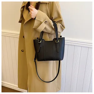 Classic black pebbled leather tote bag with gold rings shown on a khaki trench coat
