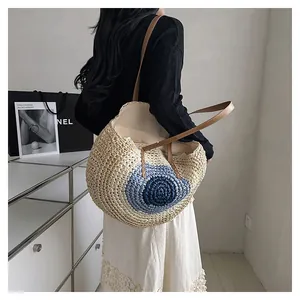 Detail of round straw tote bag featuring blue circular pattern and brown leather straps
