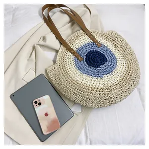 Flat lay of woven evil eye tote bag with leather handles next to lifestyle items