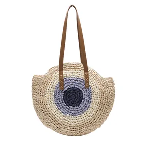 Bohemian round straw tote bag with center pattern and brown leather straps on white background