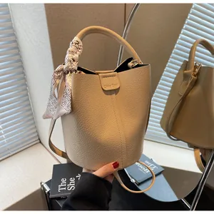 Detail of beige lychee grain bucket bag featuring silk scarf and branded flap closure