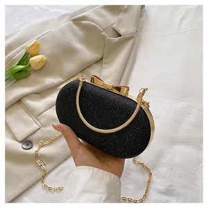 Close-up of black glitter evening clutch with golden bow clasp and metal chain