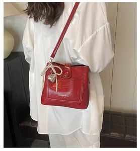 Détail d'un sac seau en cuir rouge avec nœud en perles et breloque cœur en métal