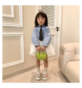Close-up of mini green chain bag with ring handle on a stylishly dressed child model