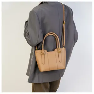 Detail view of khaki pebbled leather tote bag worn by model in a business casual outfit