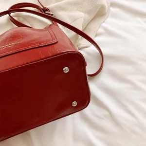 Détail du sac seau rouge montrant les pieds en métal et la texture du cuir ciré lisse