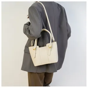 Back side view of a beige crossbody bucket bag paired with a professional grey suit