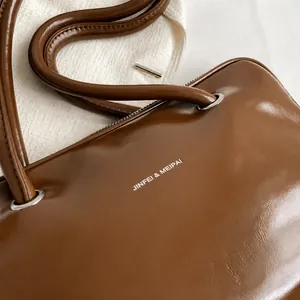 Close-up of brown textured leather shoulder bag with metallic ring and brand logo detail