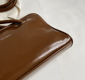 Close-up of glossy brown leather texture and silver metal hardware on underarm bag