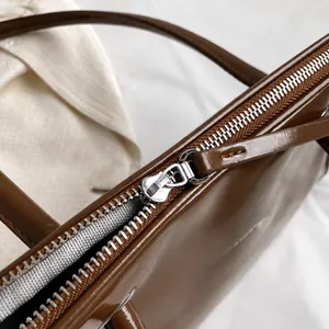Detailed macro view of the smooth metal zipper on a brown patent leather shoulder bag