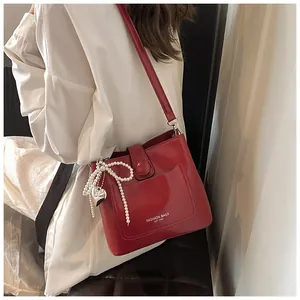 Sac seau en cuir verni rouge avec nœud en perles et breloque cœur sur une chemise blanche