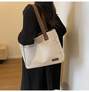 Close-up of durable canvas tote bag featuring a leather brand tag and wide brown shoulder straps