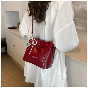 Détail du sac seau rouge foncé avec nœud en perles et pendentif cœur sur chemise blanche
