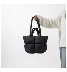 Detail of black quilted puffer tote bag held by model wearing a white mohair sweater