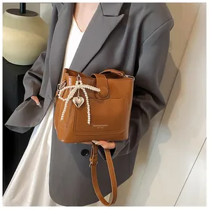 Sac seau caramel avec nœud en perles et pendentif cœur argenté porté par un mannequin