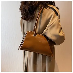 Close-up of caramel brown glossy shoulder bag with dual straps and metal logo detail