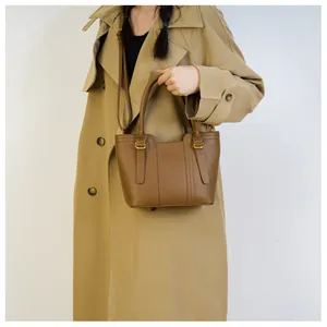Close-up of brown pebbled leather tote bag with gold hardware worn with a classic trench coat
