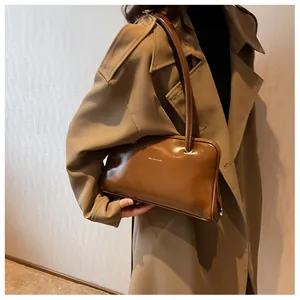 Detail of a brown glossy leather shoulder bag on model wearing a khaki trench coat