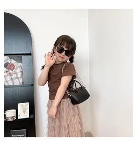 Mini black cylinder bag with silver chain worn by child with sunglasses and tutu