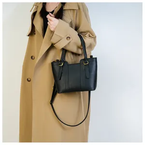 Detail of a black pebbled leather handbag with gold hardware on a beige trench coat
