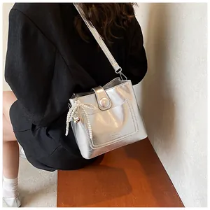 Détail du sac seau argenté avec texte embossé et breloque décorative en nœud de perles