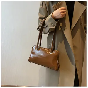 Close-up of brown glossy leather underarm bag on khaki coat showing strap detail