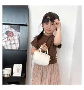Close-up of a mini cream white faux leather tote bag with metal chain on a child model