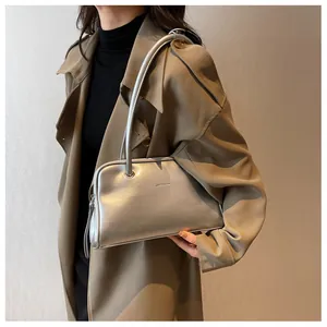 Close-up of metallic silver shoulder bag with long straps worn on a stylish brown coat