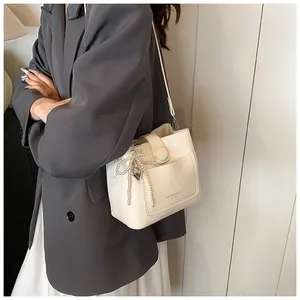 Détail d'un sac seau en cuir crème avec nœud en perles et breloque cœur sur un modèle