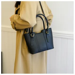 Detail of a black pebbled leather bucket bag with gold hardware and top handles