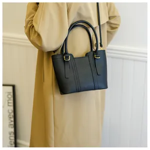 Detail of black pebbled leather bucket bag with gold hardware held by a model in a trench coat
