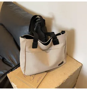Detail of a minimalist canvas tote bag with black strap and exterior pocket on stone base