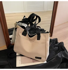 Detail of beige canvas tote bag with black strap, gold metal hardware and brand label
