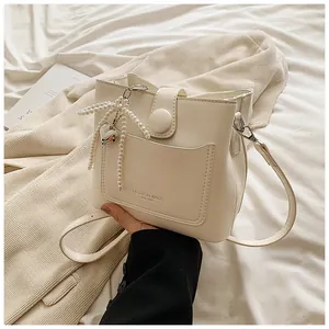 Détail du sac seau crème avec pendentif cœur et nœud en perles sur un lit doux