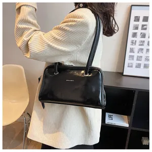 Detail of black glossy faux leather underarm bag featuring dual straps and brand logo