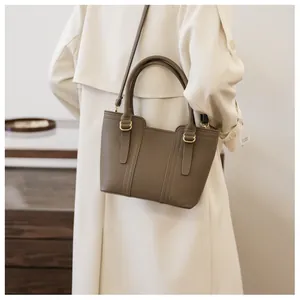 Detail of dark khaki pebbled leather bucket bag with gold hardware on a beige trench coat