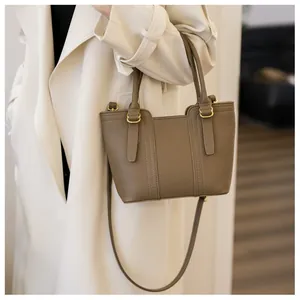 Close-up of pebble leather texture and golden hardware on taupe handbag worn with trench coat