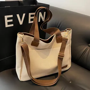 Minimalist canvas tote bag in off-white with brown straps on a dark leather sofa