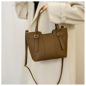 Detail of brown lychee texture leather handbag with gold metal clasp on a beige coat