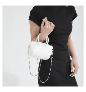 Close-up of white mini Boston bag with silver chain strap on black dress