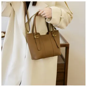 Close-up of brown leather bucket bag with top handles and shoulder strap worn by model