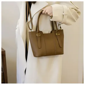 Brown grainy leather tote bag shown on a model wearing a beige trench coat for commute