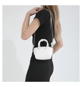 Close-up of mini white handbag with round handle and silver ball chain strap detail