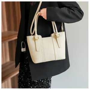 Detail of cream pebbled leather handbag with gold hardware worn by a model in black blazer