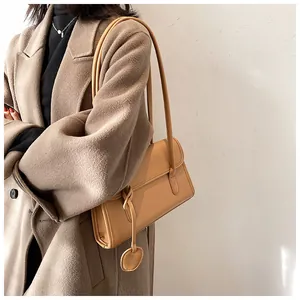 Detail of light brown leather underarm bag with matching circular charm and thin straps