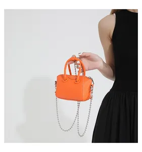 Detail of mini orange leather handbag featuring a silver ball chain and trapezoid shape