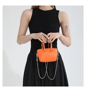 Detail of a bright orange leather mini handbag worn with a metallic chain strap