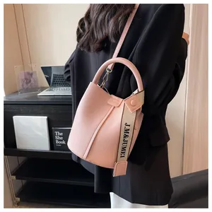 Gros plan d'un sac seau en cuir rose avec sangle en toile de marque sur un bureau